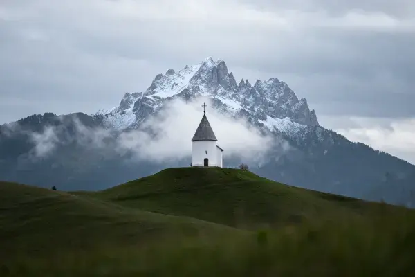 山间草丘上的乡村小教堂与雪山景致
