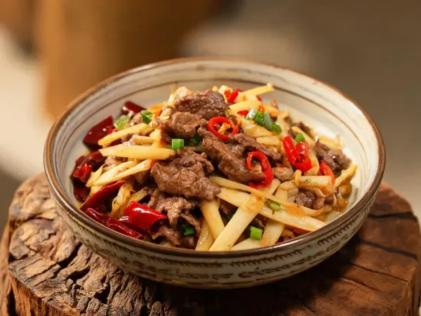牛肉炒茭白菜品中,棕褐色牛肉片与白色茭白条相互搭配,盘中点缀着红色辣椒圈。