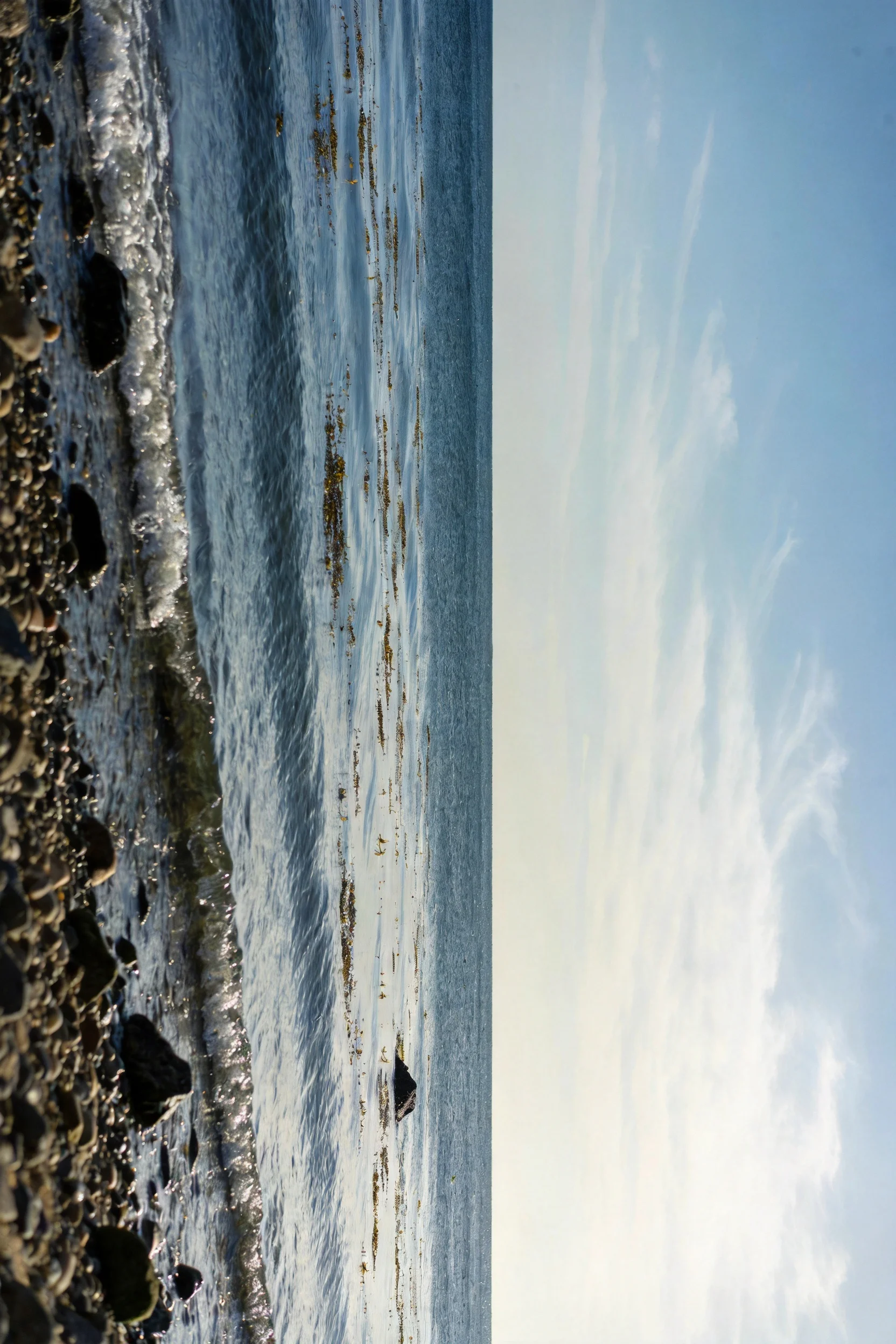 海岸礁石风光展现,海水泛起细碎浪纹,礁石表面带有潮湿痕迹,天空澄澈湛蓝。