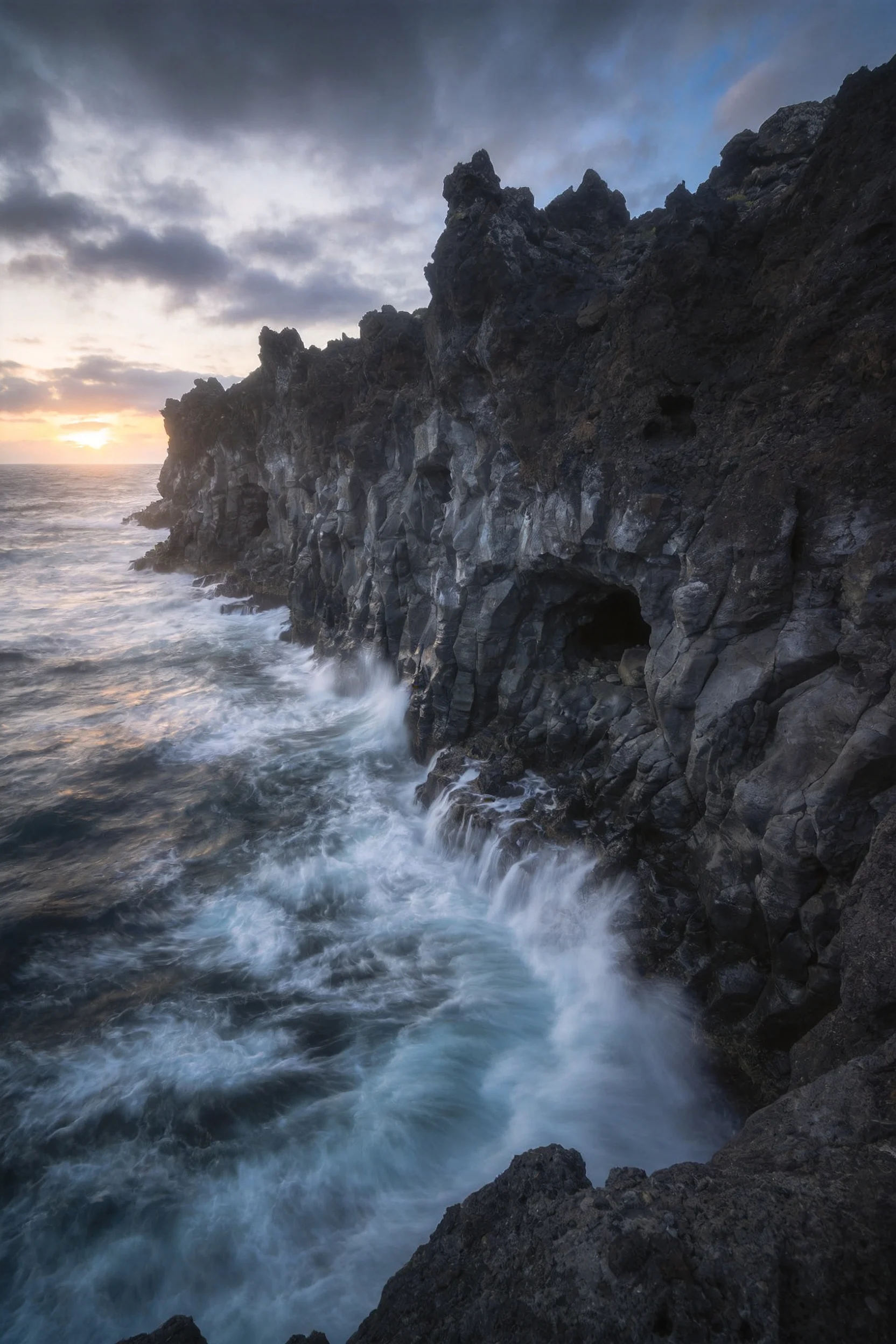 火山岩海岸峭壁上,海浪撞击处泛起大量白色泡沫,黑色岩石表面有明显的纹理和洞穴结构。