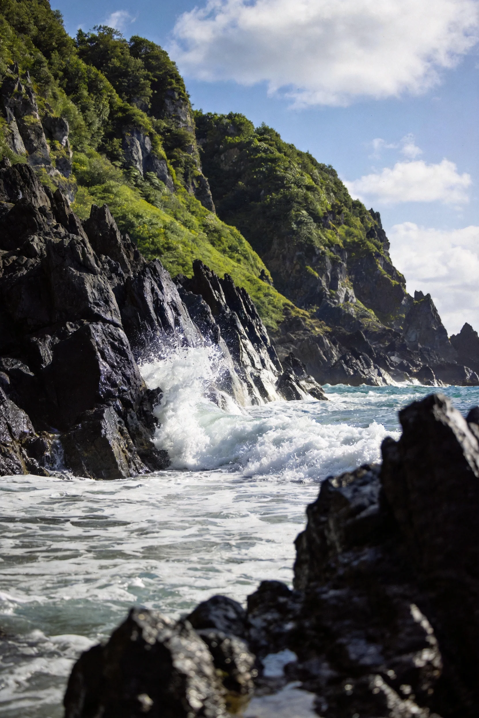 海岸火山岩礁上，白色浪涛有力撞击黑色礁石，礁石表面粗糙有棱角，海水呈蓝绿色，展现景观原始风貌。