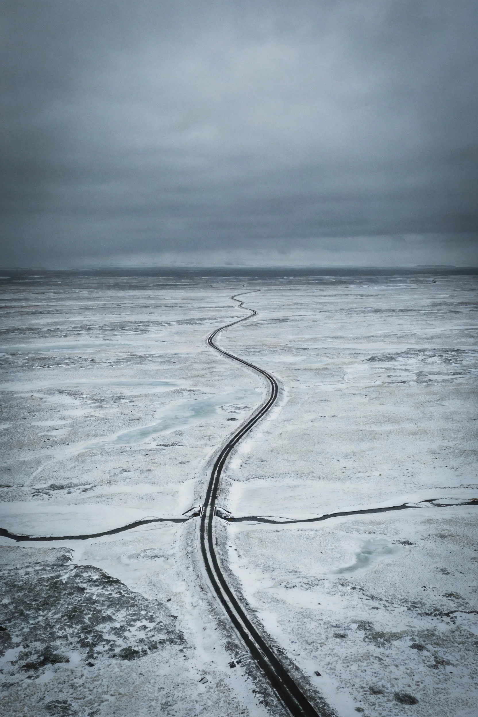 阴天下的冰雪铁路景观,深色铁轨与白色雪景形成鲜明对比,铁轨纹理清晰可见。