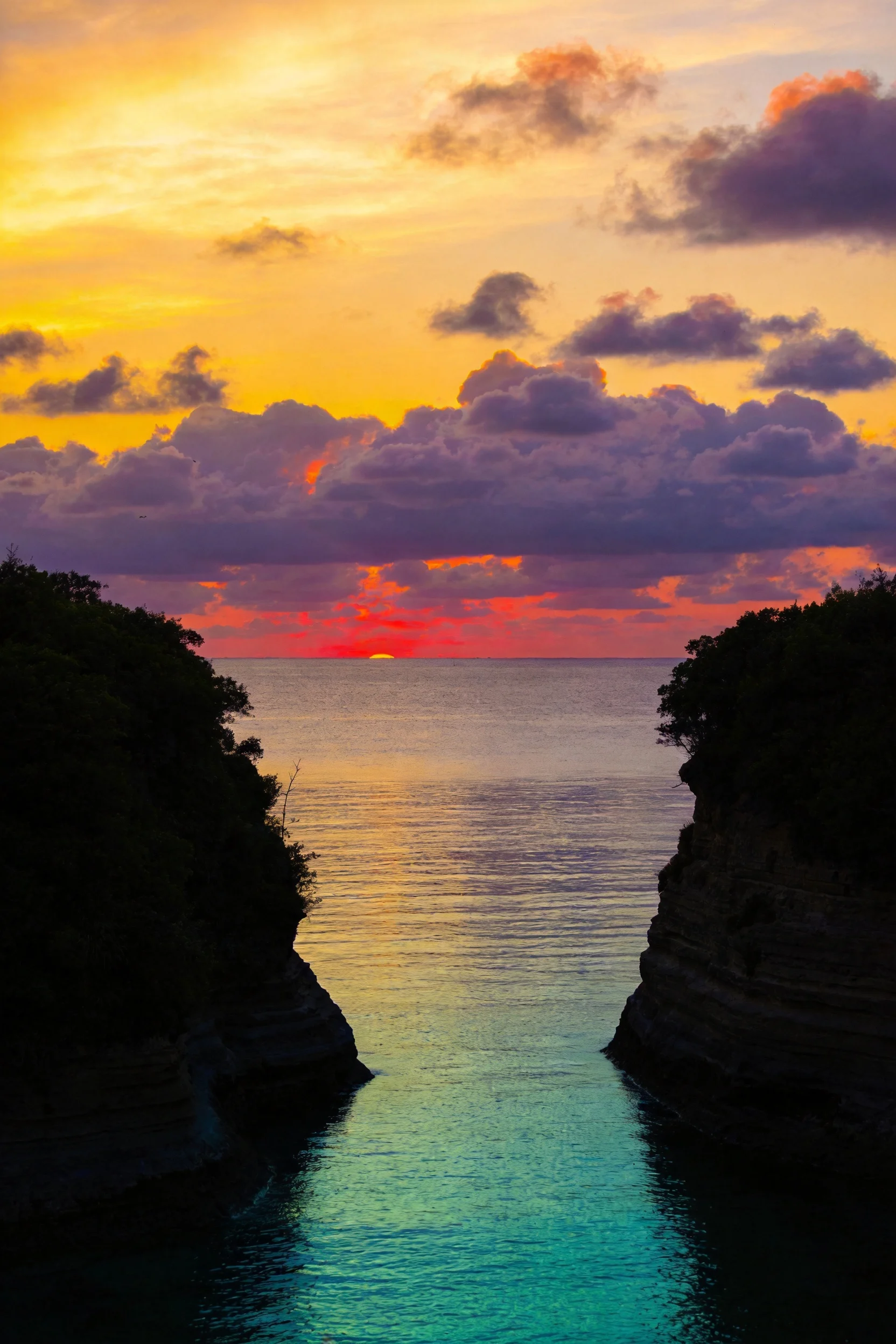 沿海峡谷地貌中,橙红色天际线映照在碧绿色水道上,两侧峭壁夹峙形成天然通道。