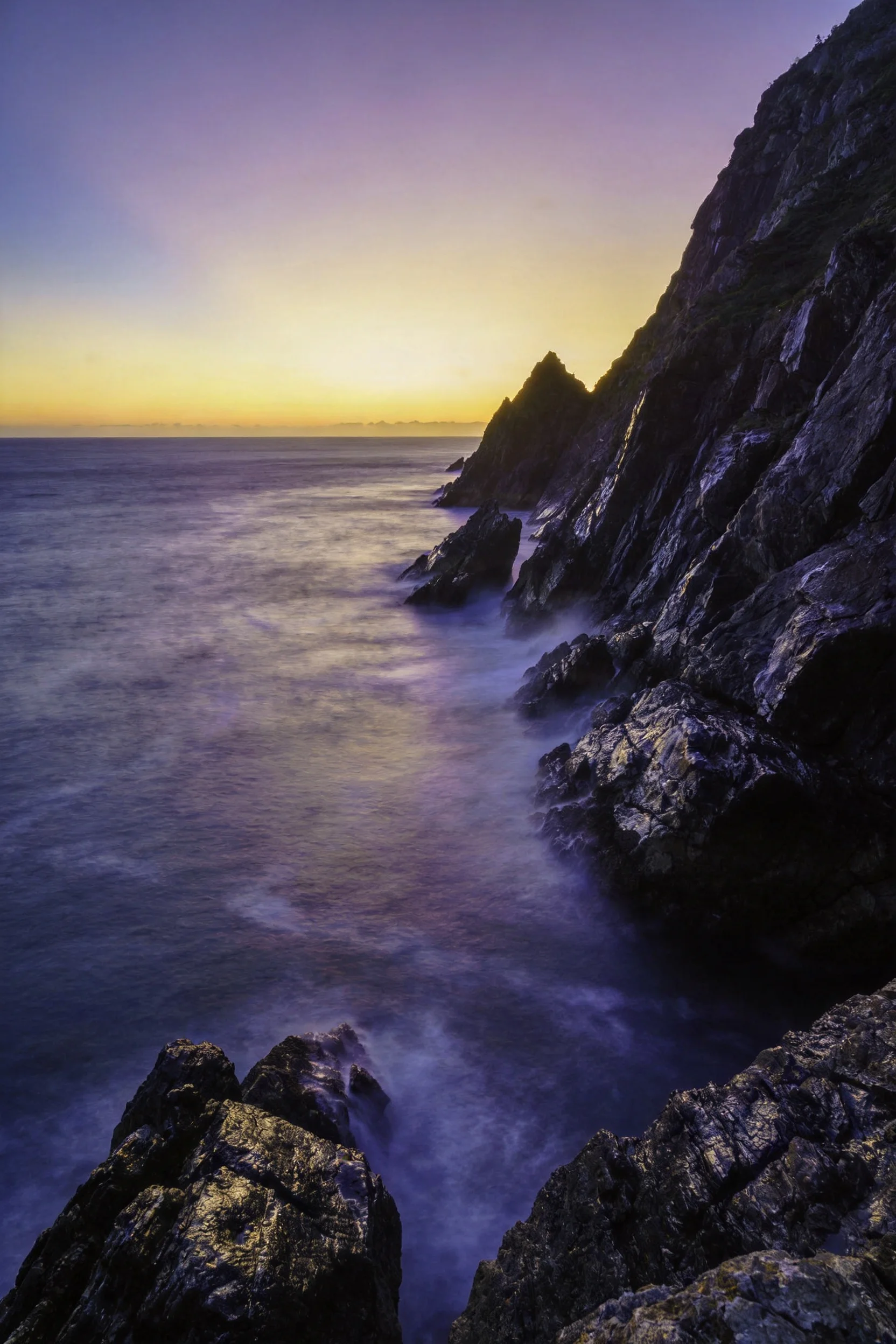 海岸悬崖景观中黑色纹理表面有粗糙纹理,海水呈淡蓝色且略显朦胧。