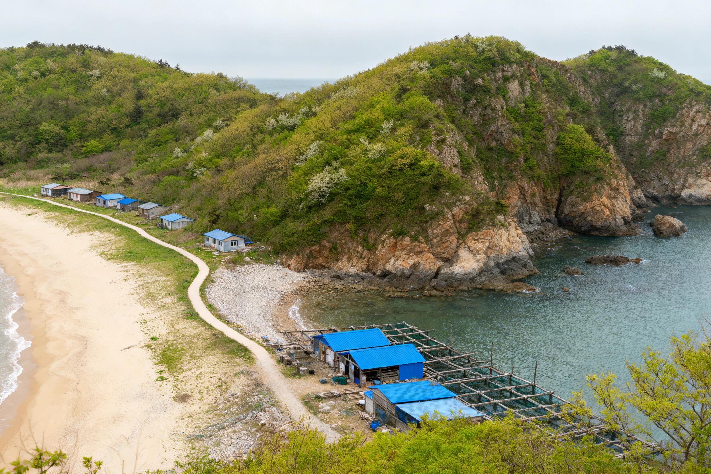 沿海岩崖渔村中蓝色养殖设施靠近海边,设施框架结构清晰可见。