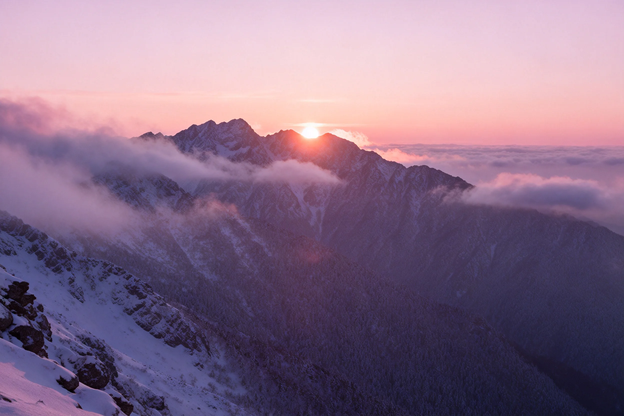 高山雪景里,晨阳从主峰后方升起,粉紫天空下云雾环绕,雪地表面有细腻的纹理。