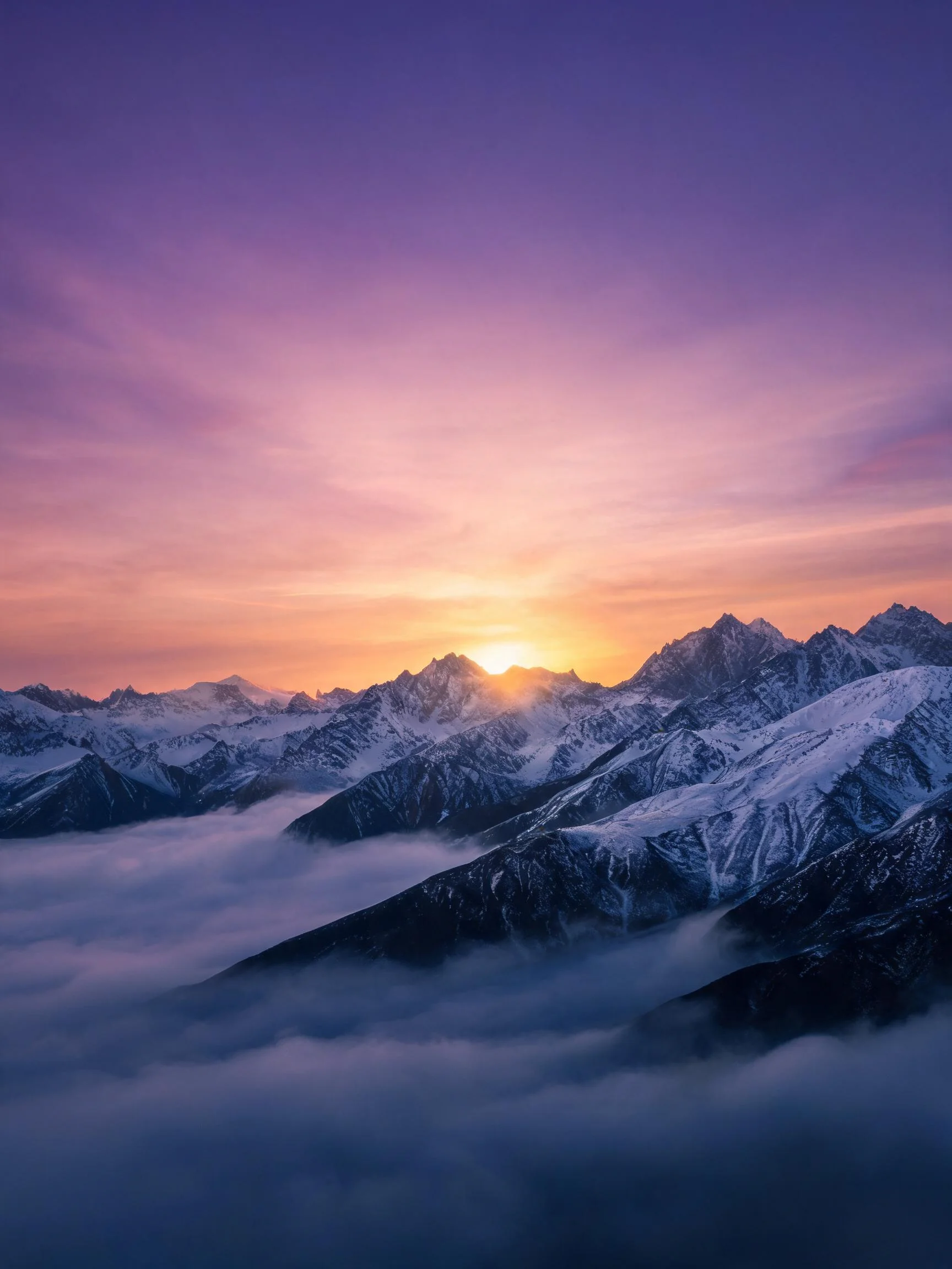 雪山风光中,夕阳的金色光芒洒落在银白的山峰上,云层在山谷间形成朦胧的雾霭,展现出的壮丽景象。