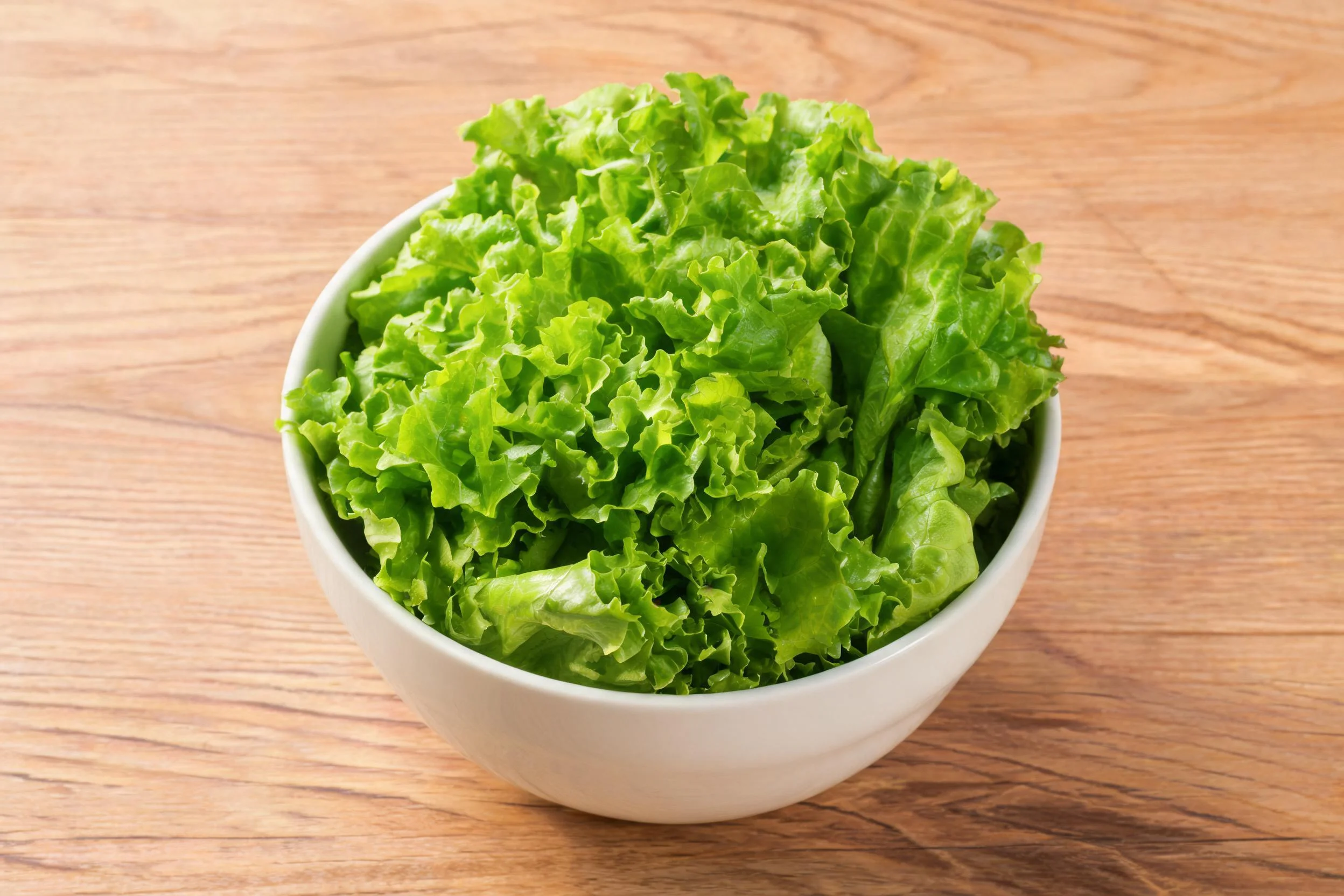 白色碗内的生菜叶片饱满,呈现出鲜亮的绿色,叶片边缘有的波浪形褶皱。